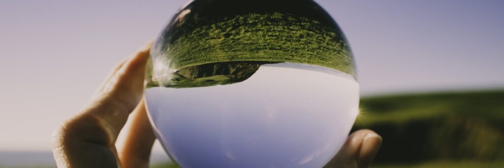 Hand holding a reflective glass sphere outdoors.